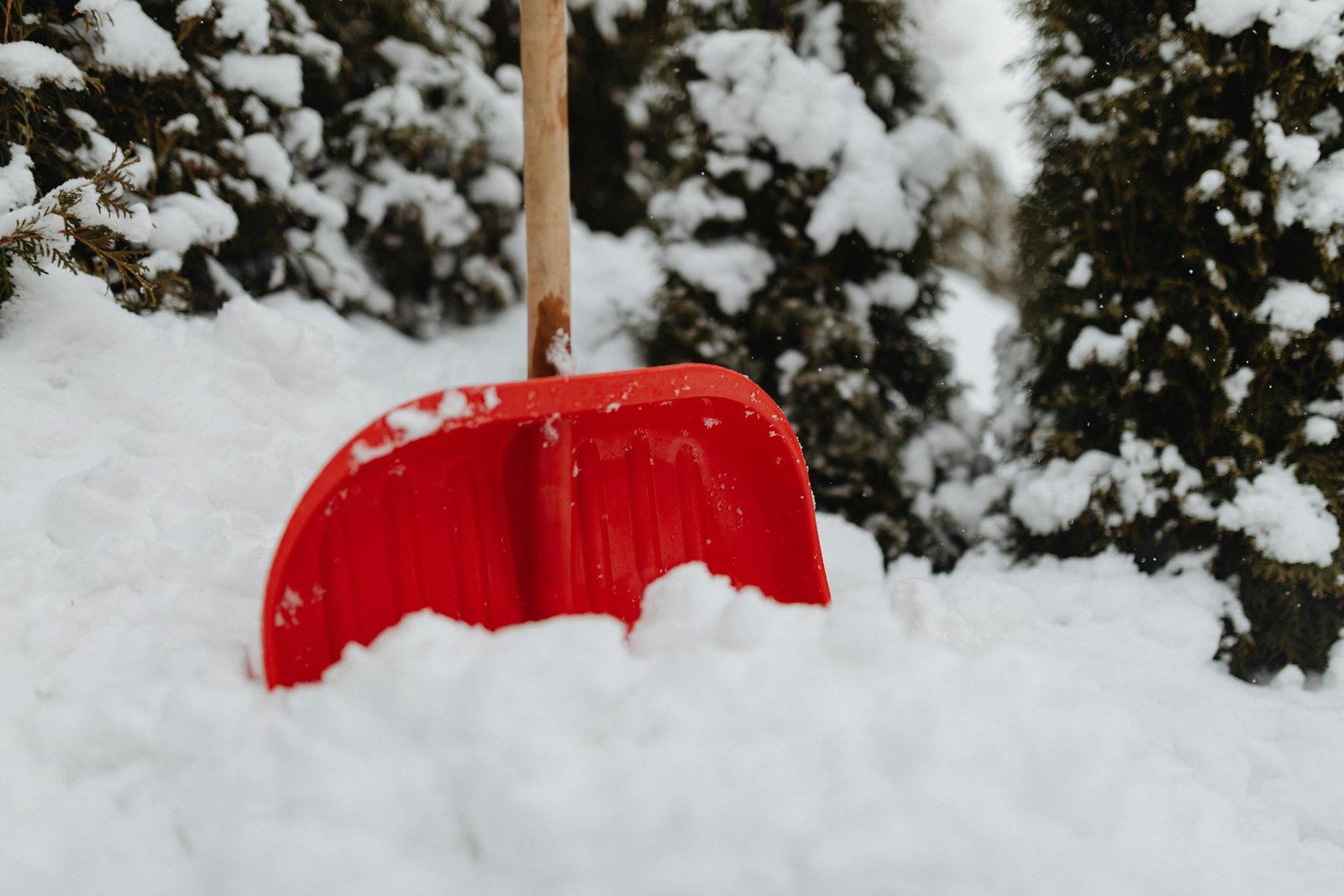 Close-up of a red snow shovel amidst heavy snowfall outdoors.